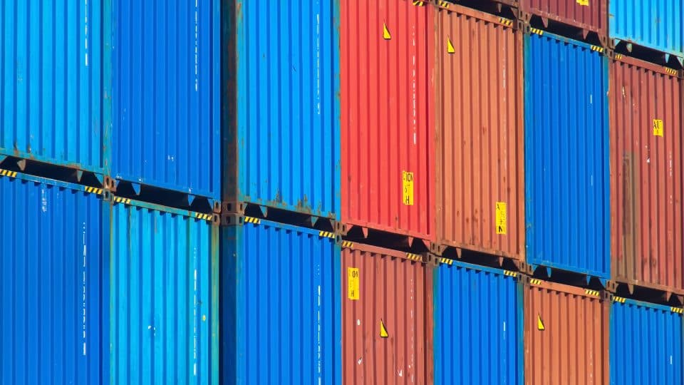 Stacked, standardized shipping containers in blue, red and orange, each sealed and numbered separately.