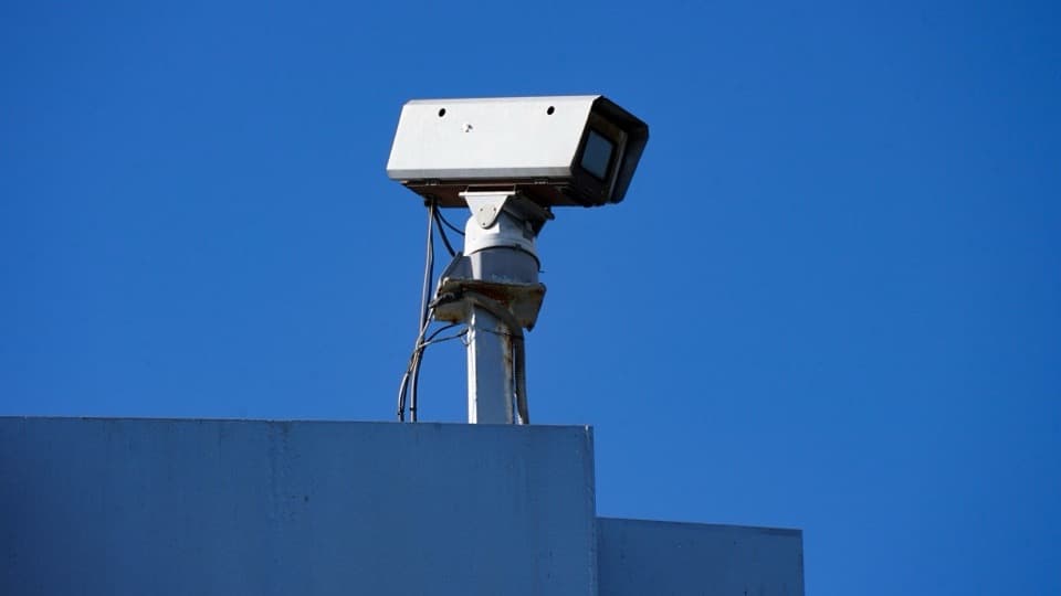 A security camera mounted on the roof of a building against a clear blue sky.