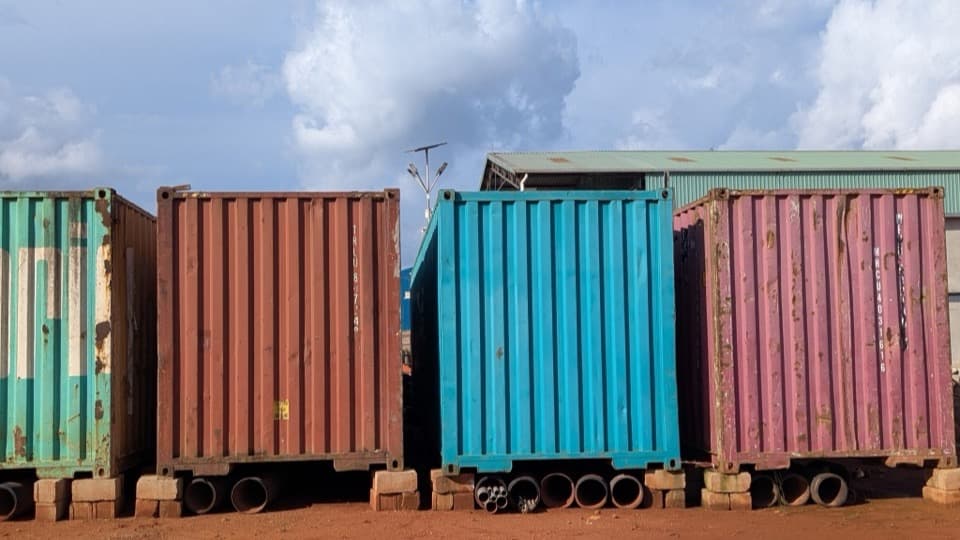 A row of closed, weathered shipping containers in a yard under a cloudy sky.
