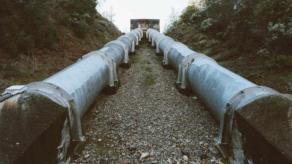 Two parallel steel pipelines running down a gravel channel toward a shared outfall in the distance.