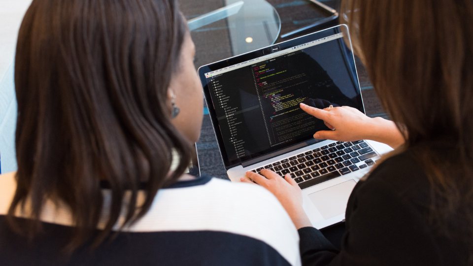 Two developers reviewing code together on a laptop.