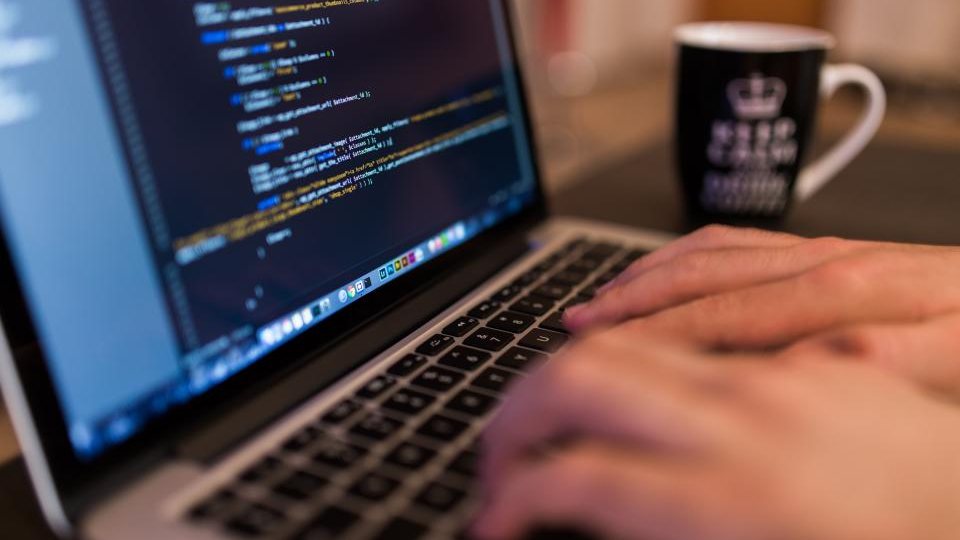Hands typing on a laptop with source code on screen.