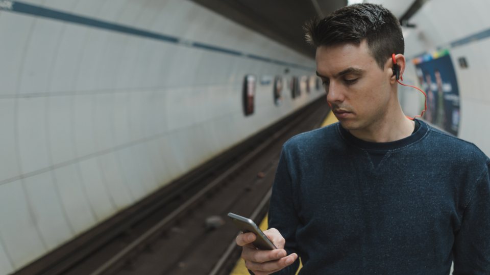 A commuter on an underground platform looking at his phone, the kind of patchy connection real users load your page on.